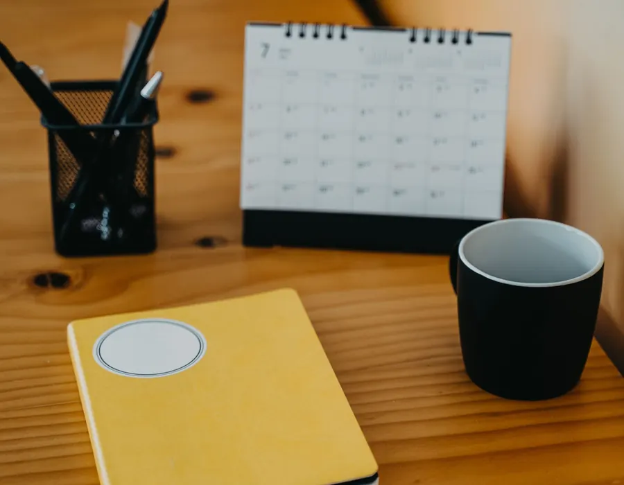 Wandkalender, gelbes Notizbuch und Tasse auf einem Holztisch