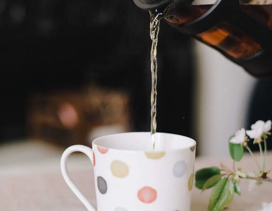 Tee wird aus einer Kanne in eine gepunktete Tasse gegossen