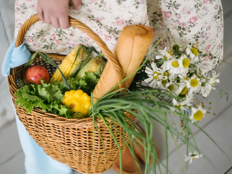 Weidenkorb gefüllt mit frischem Gemüse, Brot und Blumen