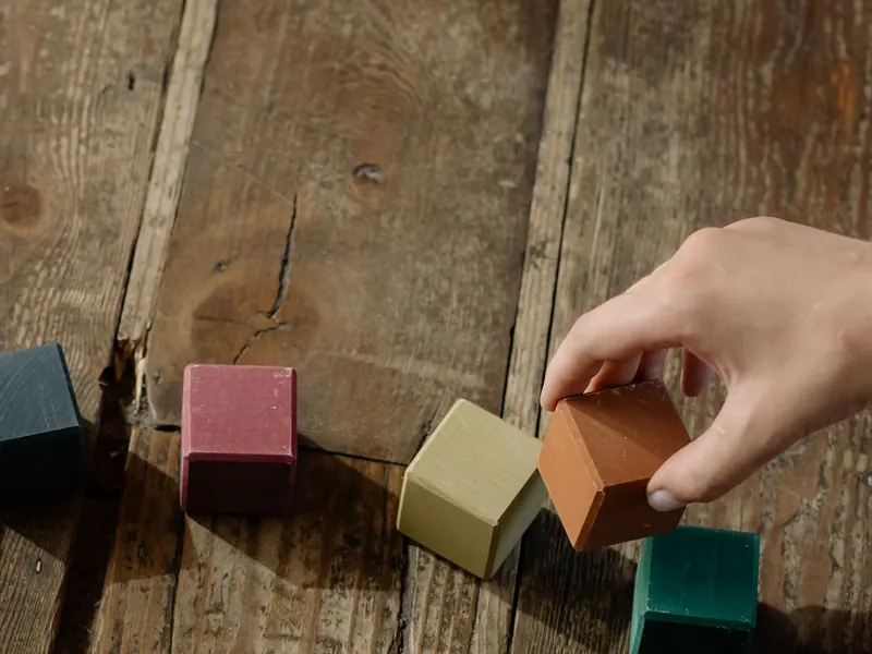 Kinderhand stapelt bunte Holzbausteine auf einem Holztisch