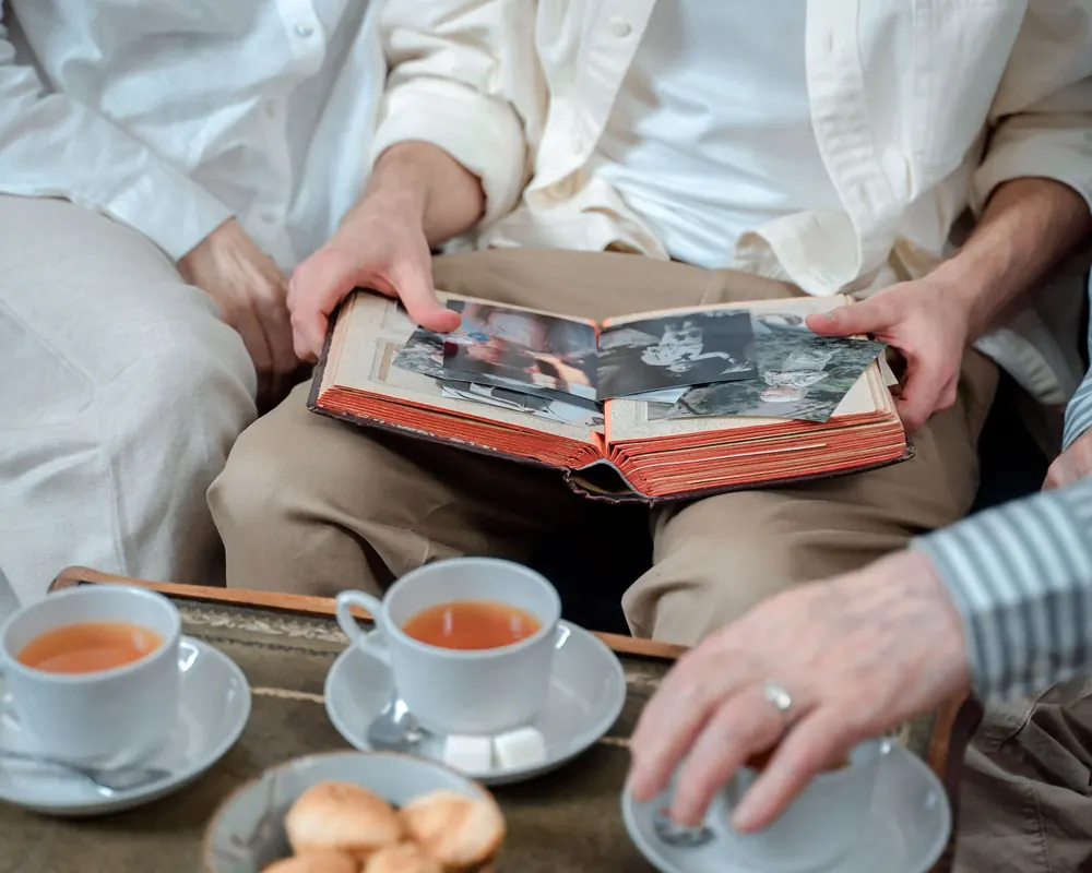 Zwei Menschen sitzen mit einem Fotoalbum und Teetassen beisammen